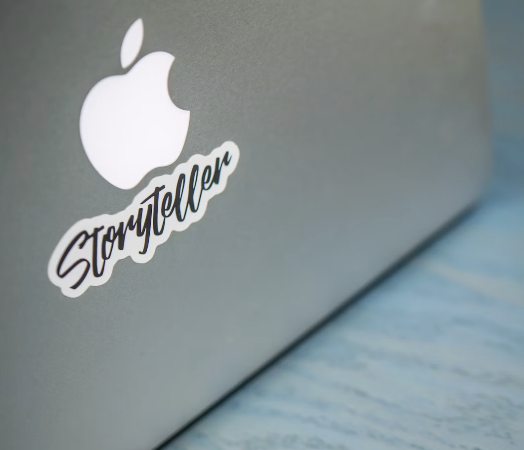 Laptop lid featuring a script Storyteller sticker placed below the illuminated logo.