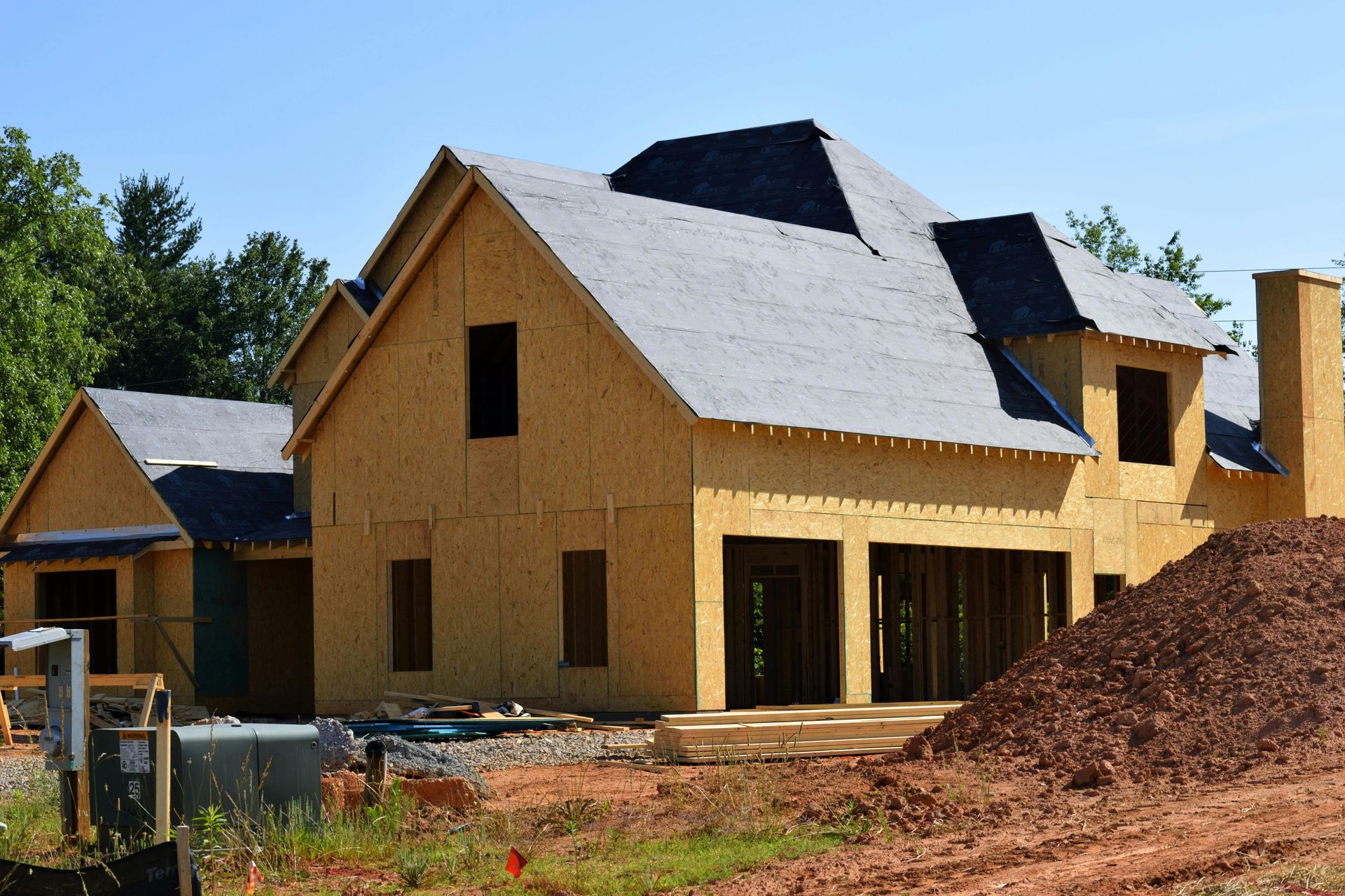 A two-story house under construction with plywood walls and black roof underlayment.